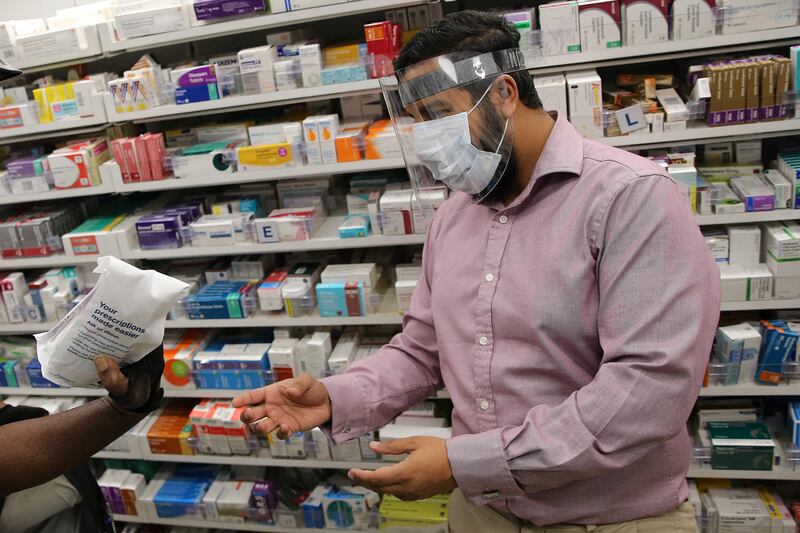 (FILES) In this file photo taken on April 17, 2020 A pharmacist at a Boots Pharmacy, in PPE including a full face mask as a precautionary measure against COVID-19, passes a completed prescription to Bikeworks cycling instructor Jelil Adebiyi (L), for him to to deliver to vulnerable people as part of the Bikeworks Cycle Delivery Service (COVID-19) in east London on April 17, 2020.  - British pharmacies Boots are launching a new service in 14 UK cities, including London and Edinburgh, to deliver medicines and cosmetics by courier with the Deliveroo platform.  (Photo by ISABEL INFANTES  /  AFP)