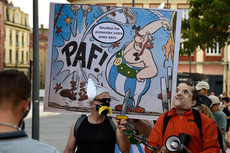 A protester holds a placard depicting French cartoon character Obelix that reads 'please show me your sanitary pass' as he takes part in a national day of protest against the compulsory Covid-19 vaccination for certain workers and the compulsory use of the health pass called for by the French government in Metz on August 14, 2021.  (Photo by JEAN-CHRISTOPHE VERHAEGEN  /  AFP)