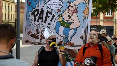 A protester holds a placard depicting French cartoon character Obelix that reads 'please show me your sanitary pass' as he takes part in a national day of protest against the compulsory Covid-19 vaccination for certain workers and the compulsory use of the health pass called for by the French government in Metz on August 14, 2021.  (Photo by JEAN-CHRISTOPHE VERHAEGEN  /  AFP)