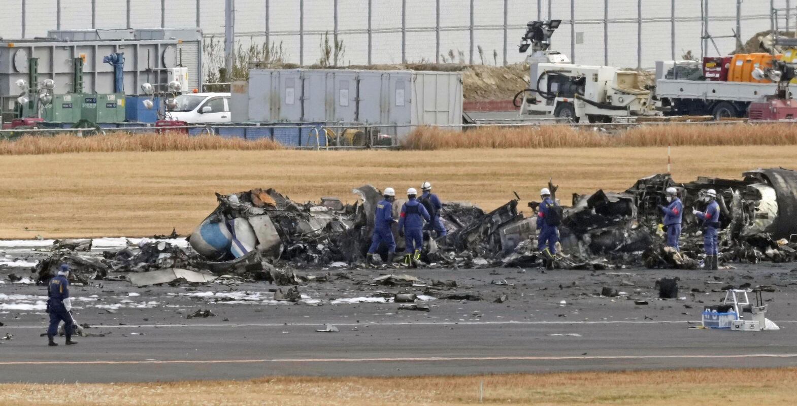 Firefighters gather around the burn-out Japanese coast guard aircraft at Haneda airport on Wednesday, Jan.  3, 2024, in Tokyo, Japan.  Transport officials and police each began their on site investigation at Tokyo’s Haneda Airport on Wednesday after a large passenger plane and the Japanese coast guard aircraft collided on the runway and burst into flames, killing several people aboard the coast guard plane.  (Kyodo News via AP)