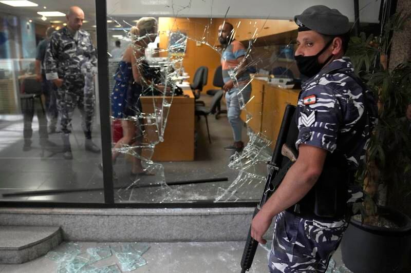 A Lebanese policeman stands guard next to a bank window that was broken by depositors to exit the bank after attacking it trying to get blocked money. A Lebanese activist group said they will continue to organize bank raids to help people retrieve their trapped savings. AP