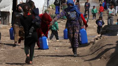Syrian refugees walk as they carry containers at an informal tented settlement in the Bekaa valley, Lebanon. Reuters
